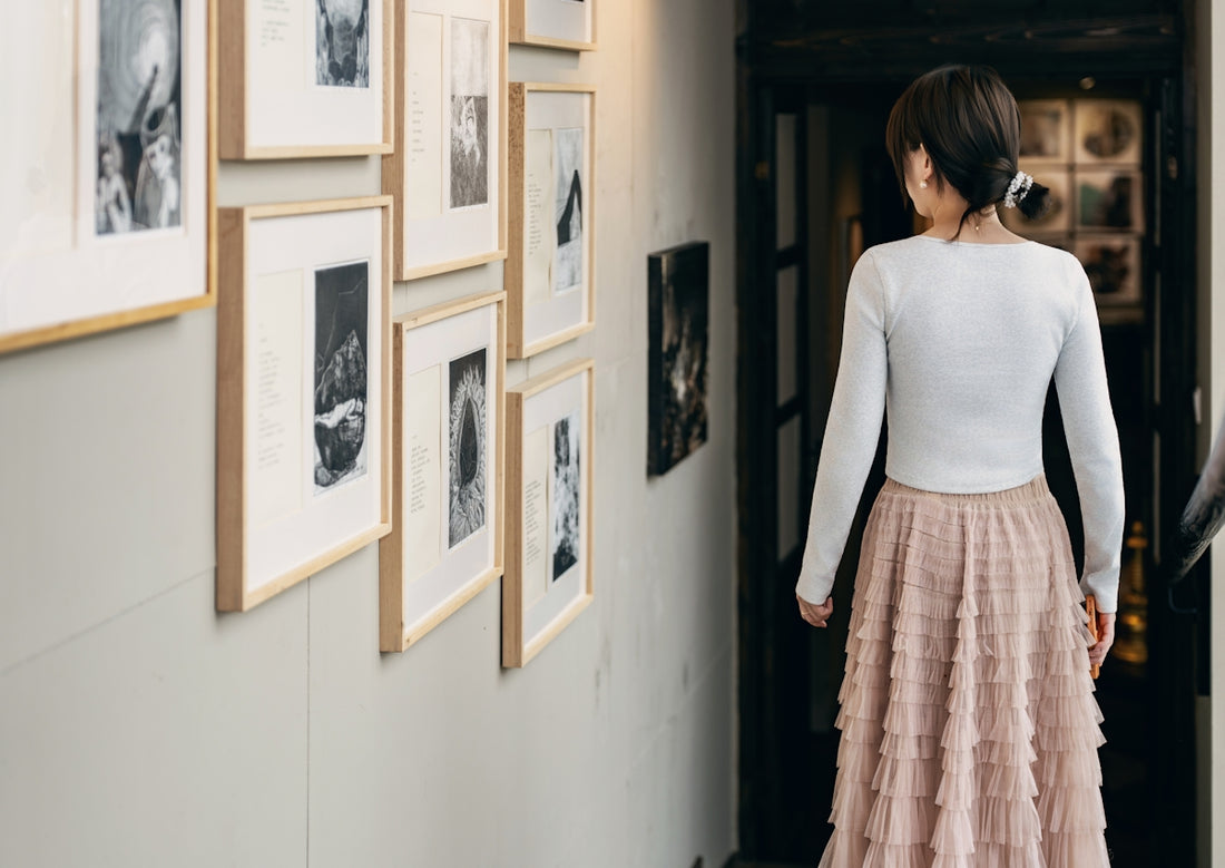 Woman in a long skirt walks past framed artwork.