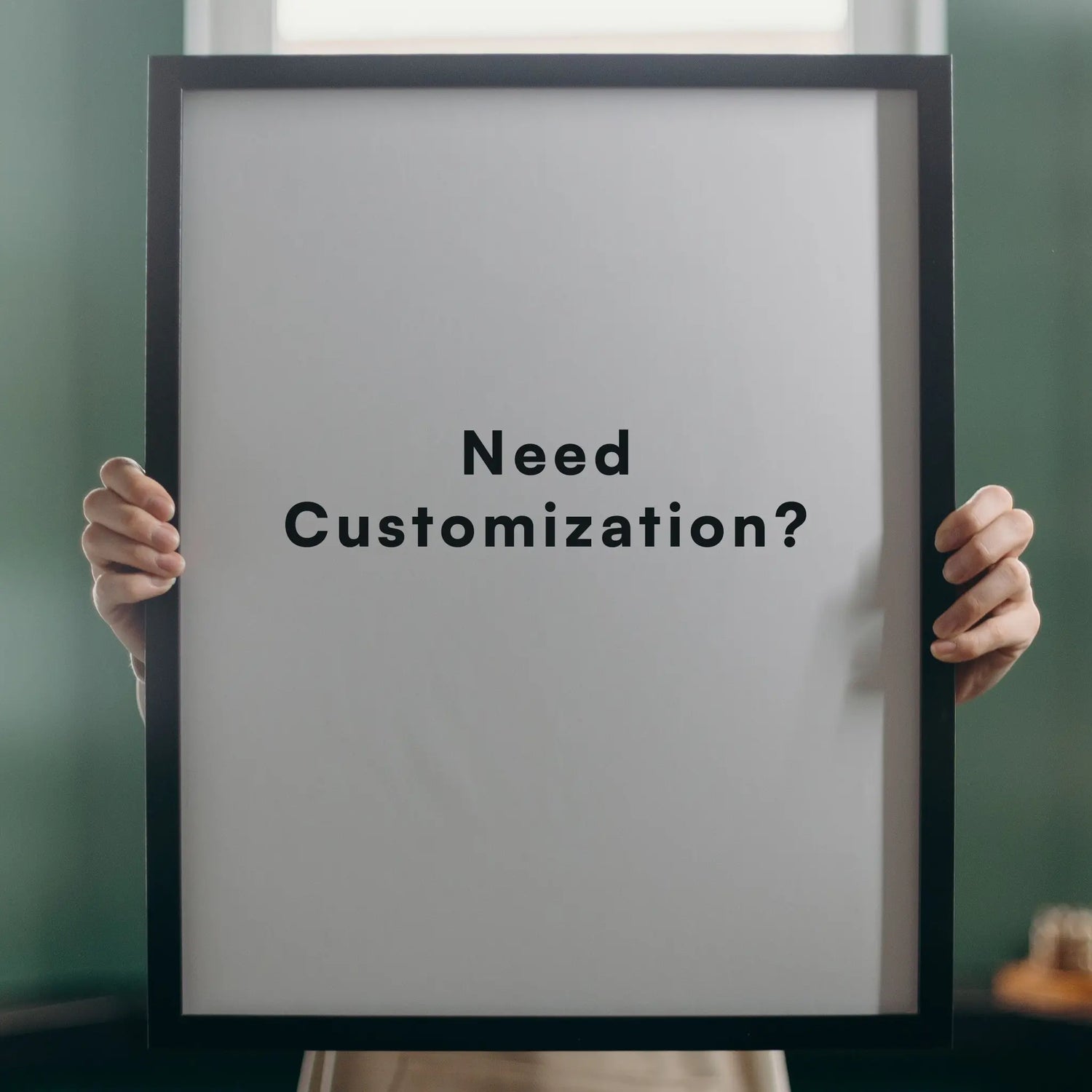 Person holding a framed poster with 'Need Customization?' text against a green wall.